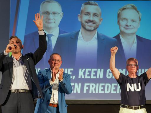 AfD-Politiker Ulrich Siegmund (links), Tino Chrupalla und Kabarettist Uwe Steimle stehen lächelnd und klatschend auf einer Bühne, dahinter ist ein großes Foto mit den dreien zu sehen AfD-Politiker Ulrich Siegmund (links), Tino Chrupalla und Kabarettist Uwe Steimle stehen lächelnd und klatschend auf einer Bühne, dahinter ist ein großes Foto mit den dreien zu sehen