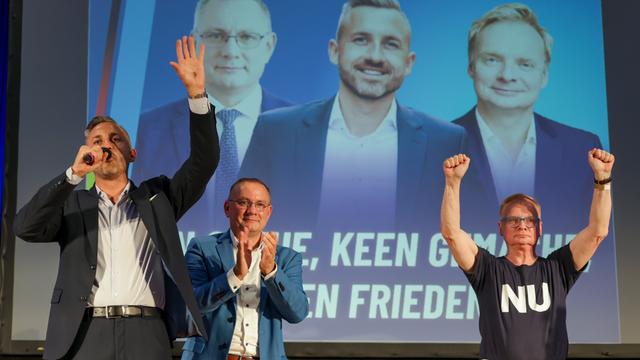 AfD-Politiker Ulrich Siegmund (links), Tino Chrupalla und Kabarettist Uwe Steimle stehen lächelnd und klatschend auf einer Bühne, dahinter ist ein großes Foto mit den dreien zu sehen 