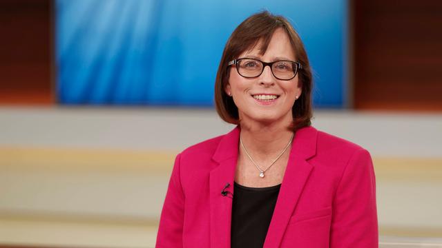 Britta Waldschmidt-Nelson sitzt in einem Fernsehstudio und schaut freundlich in die Kamera. Sie trägt Brille und ein pinkfarbenes Sakko.