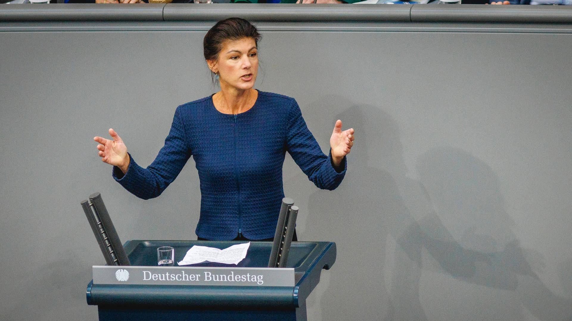 Sahra Wagenknecht steht hinter einem Rednerpult im Bundestag und breitet die Hände aus.