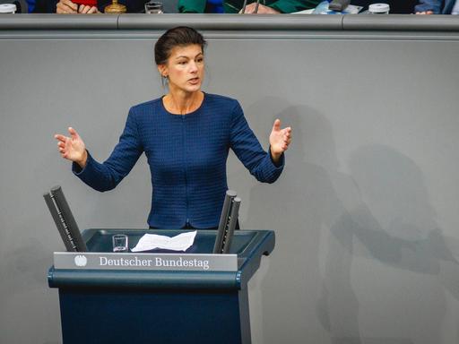 Sahra Wagenknecht steht hinter einem Rednerpult im Bundestag und breitet die Hände aus.