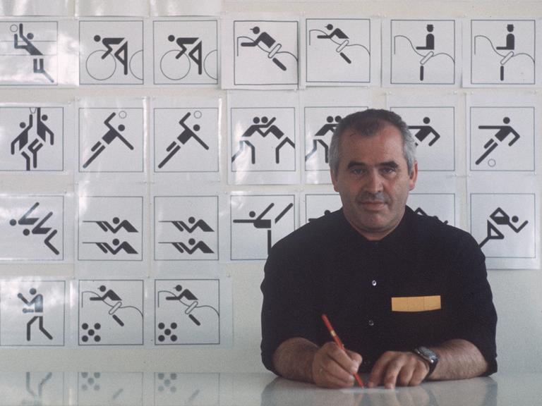 Der Grafiker, Designer, Architekt, Otl Aicher (1922-1991) sitzt 1970 an seinem Schreibtisch, im Hintergrund eine Tafel mit Piktogrammen, Symbolen, Zeichen, die er für die Sportarten der Olympischen Sommerspiele 1972 in München entworfen hat