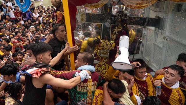 Die Prozession auf den Philippinen. Menschen drängeln sich um einen Glas-Kasten mit der schwarzen Jesus-Statue. Einige klettern an dem Glas-Kasten hoch. 