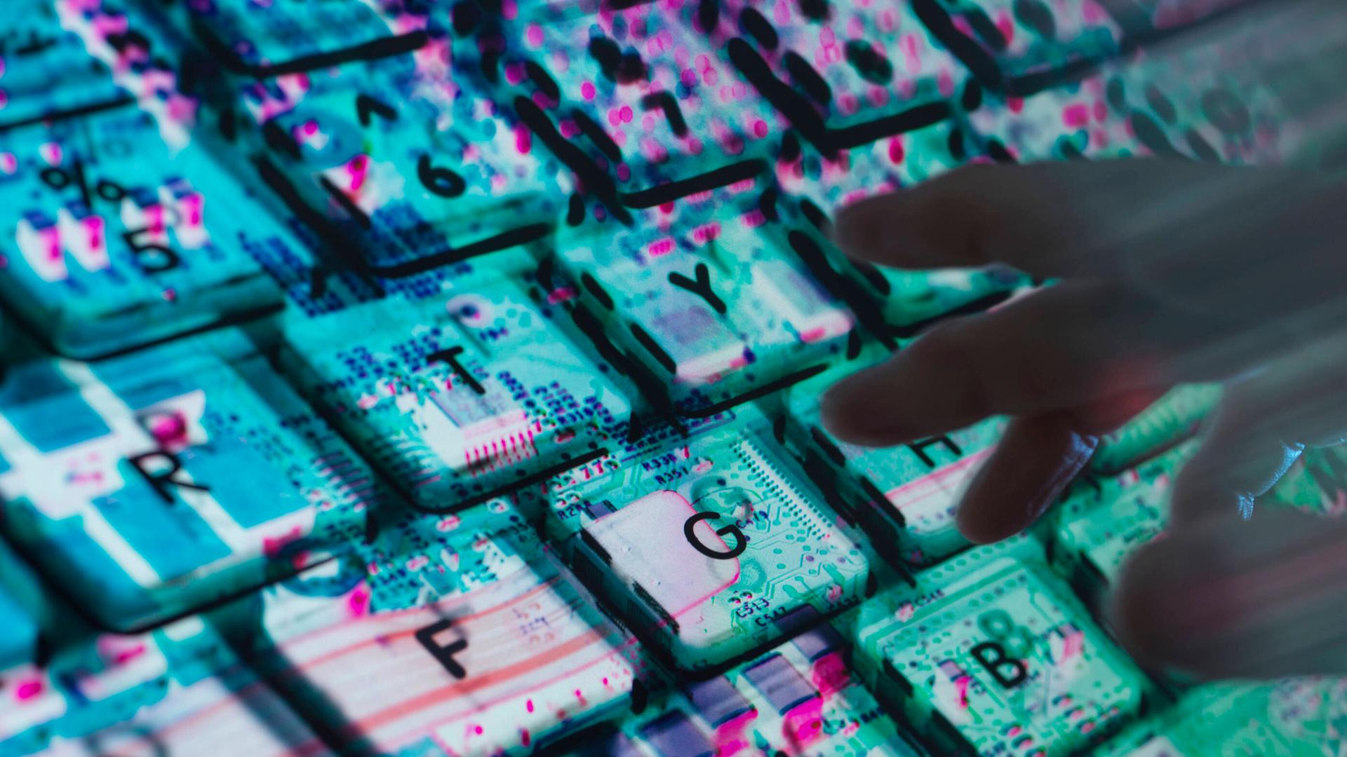 Hände tippen auf einer Computertastatur. Unter der Tastatur ist die Computerhardware zu sehen.