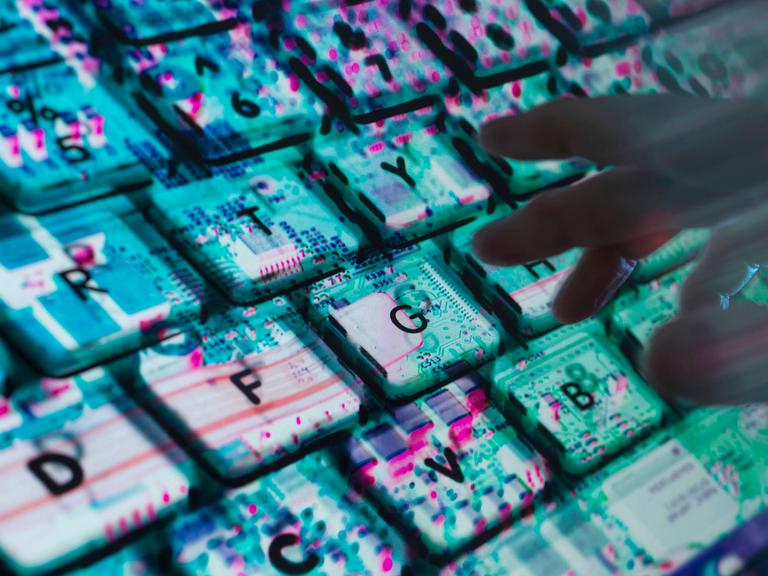 Hände tippen auf einer Computertastatur. Unter der Tastatur ist die Computerhardware zu sehen.