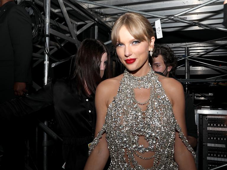 Taylor Swift bei den 2022 MTV VMAs Backstage in silber glänzendem Kleid vor schwarzem Hintergrund.