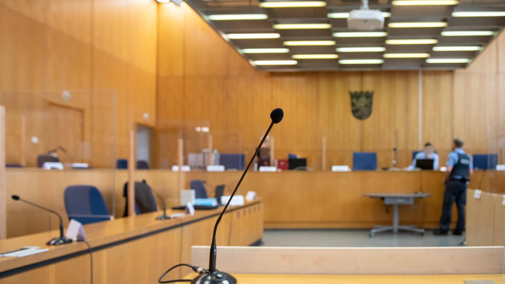 Blick in einen leeren Gerichtssaal, nur zwei Polizisten stehen an einem Tisch.