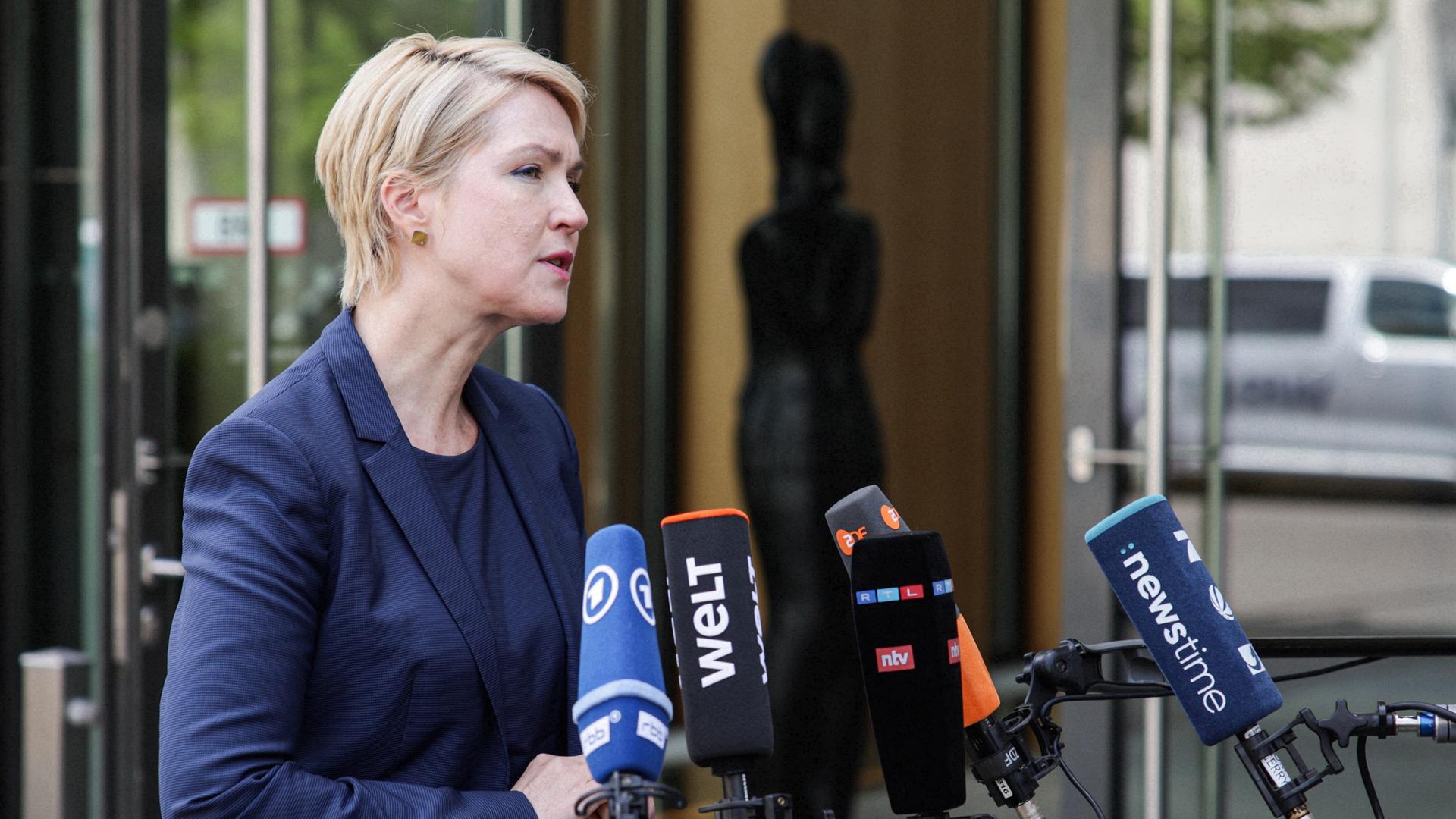 Schwesig im dunkelblauen Jackett steht vor einem Eingang und spricht in mehrere Mikrofone mit Senderlogos, die ihr entgegengehalten werden. Schwesig im dunkelblauen Jackett steht vor einem Eingang und spricht in mehrere Mikrofone mit Senderlogos, die ihr entgegengehalten werden.