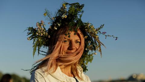 Eine Frau in weißer Tracht lächelt in die Kamera. Sie feiert die Mittsommernacht und trägt Zweige und Blätter im Haar. Eine Frau in weißer Tracht lächelt in die Kamera. Sie feiert die Mittsommernacht und trägt Zweige und Blätter im Haar.