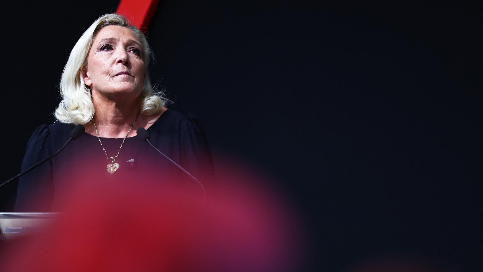 Marine Le Pen steht auf einer Bühne mit schwarzem Hintergrund.