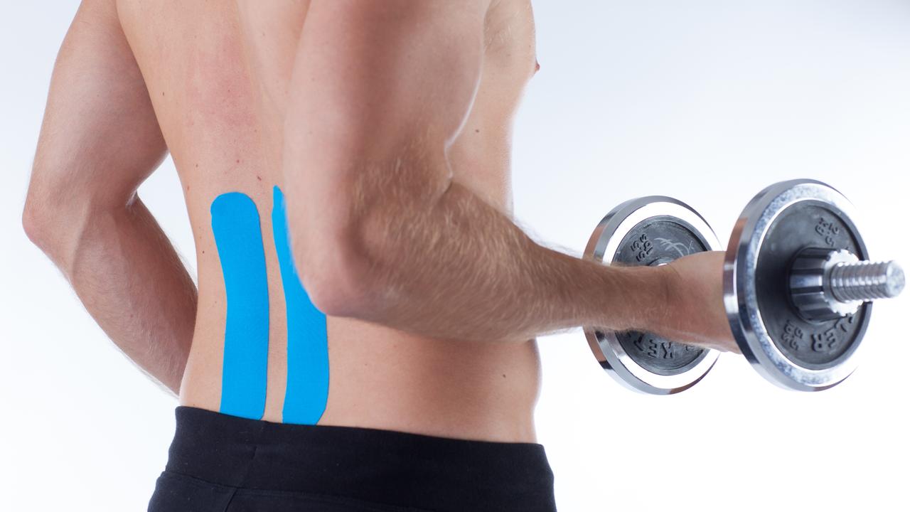 Ein junger Mann trägt ein kinesiologisches Tape am Rücken und macht dabei Bizeps-Training mit einer Kurzhantel. 