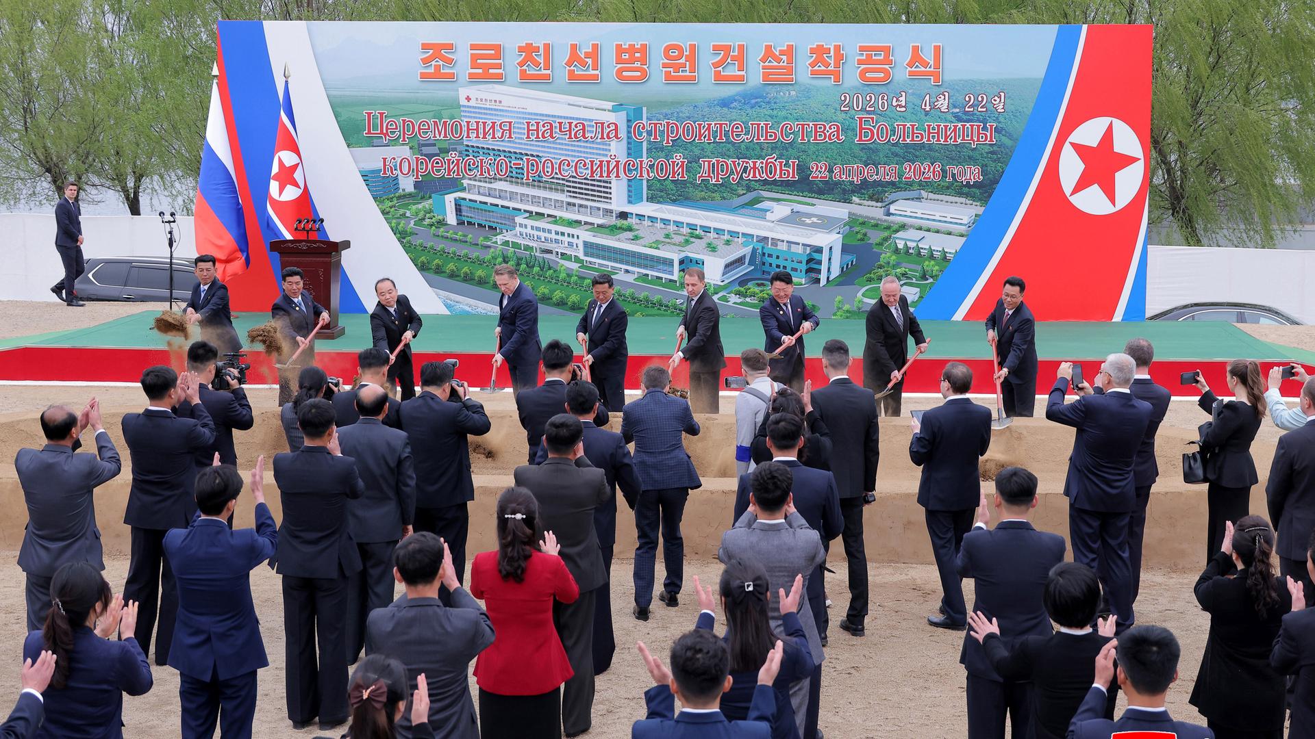 Der russische Gesundheitsminister Muraschko und weitere Vertreter nehmen an einer Feier zum ersten Spatenstich für ein nordkoreanisch-russisches Freundschaftskrankenhaus teil. Im Hintergrund ist ein Banner mit einem Bild der geplanten Klinik zu sehen.