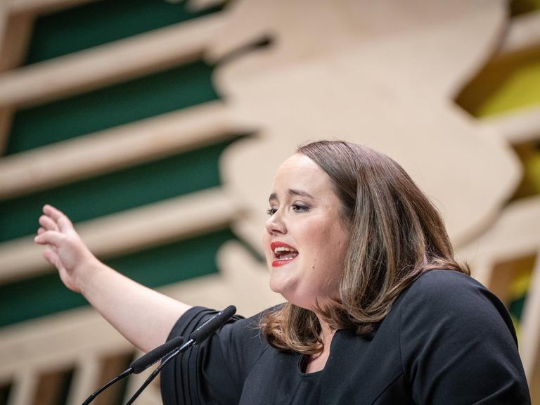 Ricarda Lang, Bundesvorsitzende von Bündnis '90/Die Grünen, hält ihre Rede vor dem Bundesparteitag. Sie spricht in ein Mikrofon und gestikuliert.