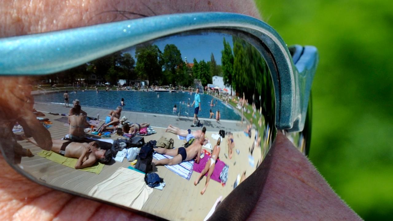 Badegäste im Schyrenbad in München spiegeln sich in der Brille eines Bademeisters.
