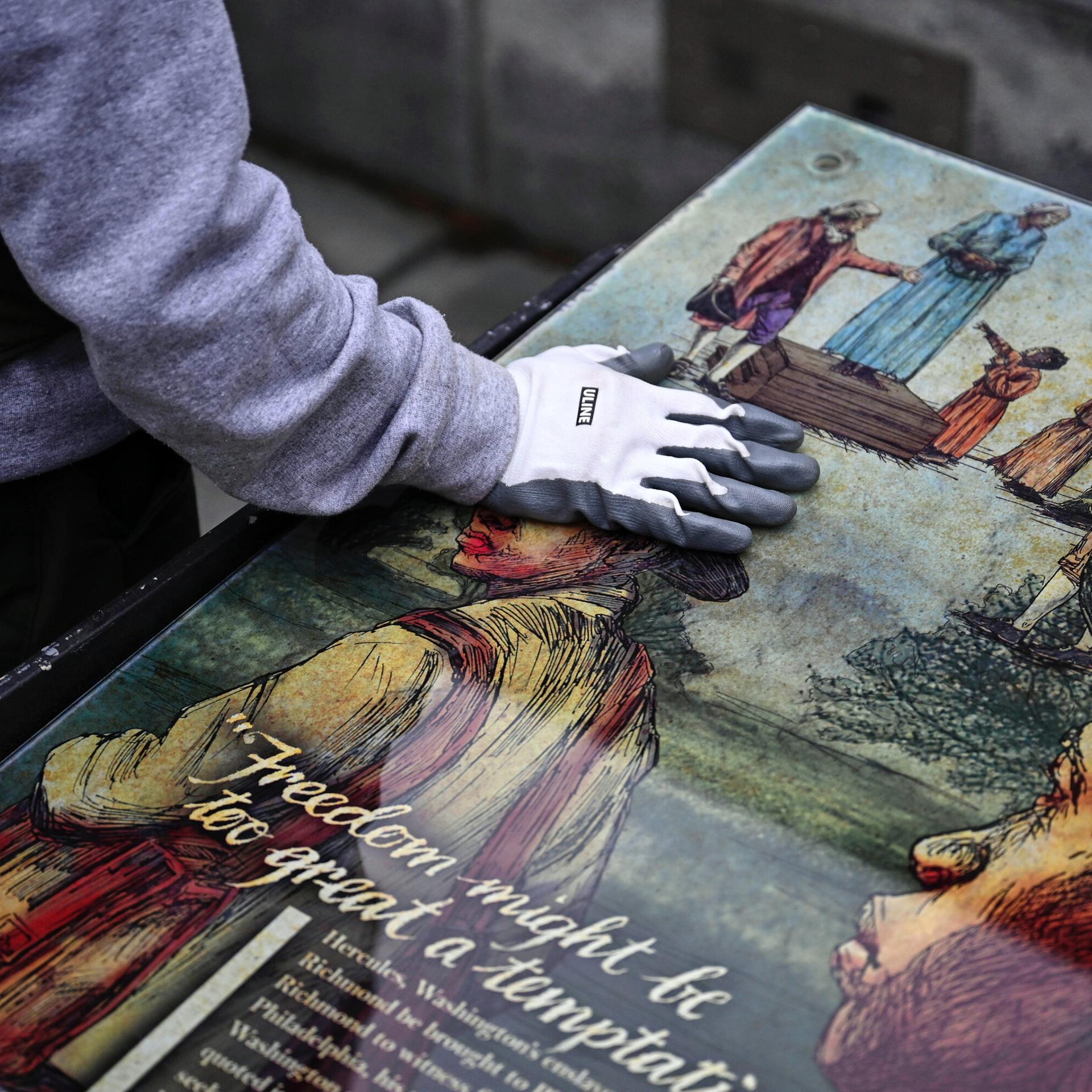 Ein Mitarbeiter des National Park Service legt seine Hand auf eine Tafel, die Teil einer Ausstellung zum Thema Sklaverei am "President’s House Site" in Philadelphia.