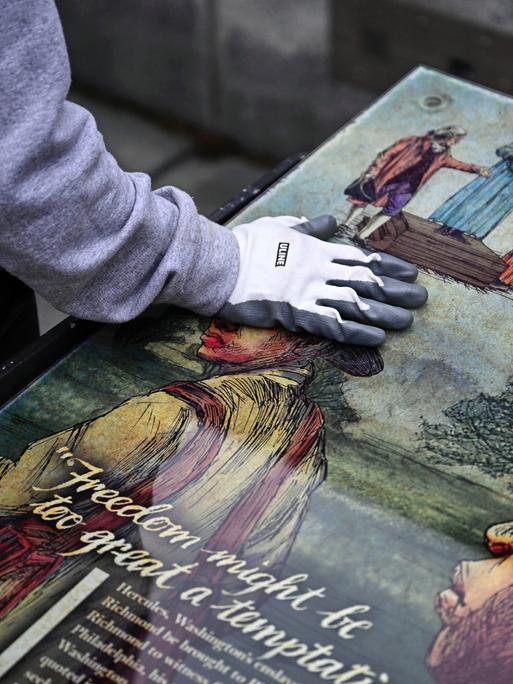 Ein Mitarbeiter des National Park Service legt seine Hand auf eine Tafel, die Teil einer Ausstellung zum Thema Sklaverei am "President’s House Site" in Philadelphia.