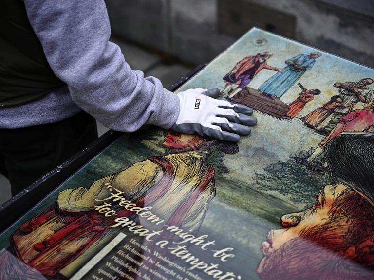 Ein Mitarbeiter des National Park Service legt seine Hand auf eine Tafel, die Teil einer Ausstellung zum Thema Sklaverei am "President’s House Site" in Philadelphia.