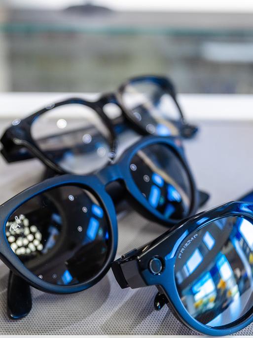 Mehrere Smart Glasses liegen nebeneinander. Einige sind blau eingefasst, eine leuchtend gelb.  
