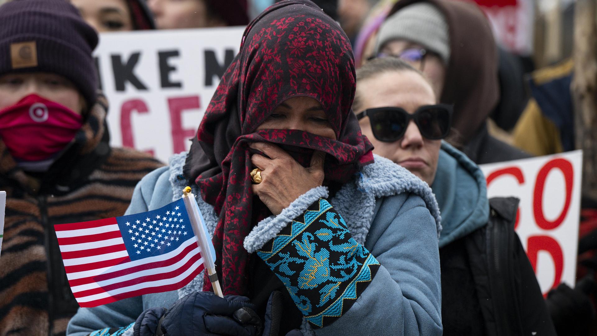 Eine Frau verdeckt mit einem Tuch ihr Gesicht. In der Hand hält sie eine kleine Fahne von den USA. 
