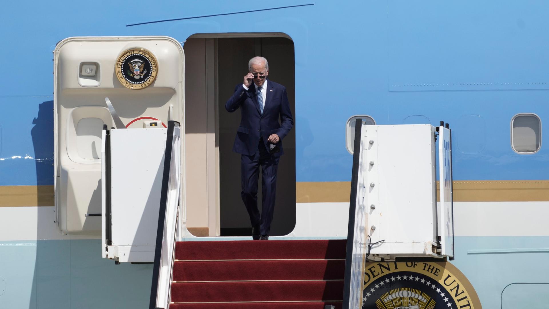 Blick von unten auf den Eingang und die Treppe. Biden setzt gerade eine Sonnenbrille auf.