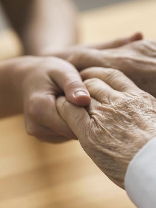 Hände einer jüngeren Frau halten die Hände eines älteren Mannesvorhanden