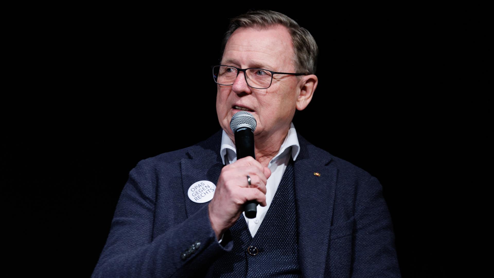 Der Ex-Ministerpräsident von Thüringen, Bodo Ramelow, sitzt bei einem Wahlkampfauftritt und hat ein Mikrofon in der Hand und hält dieses vor den Mund. 