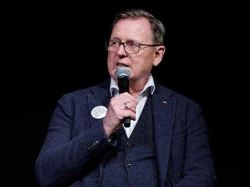 Der Ex-Ministerpräsident von Thüringen, Bodo Ramelow, sitzt bei einem Wahlkampfauftritt und hat ein Mikrofon in der Hand und hält dieses vor den Mund. 