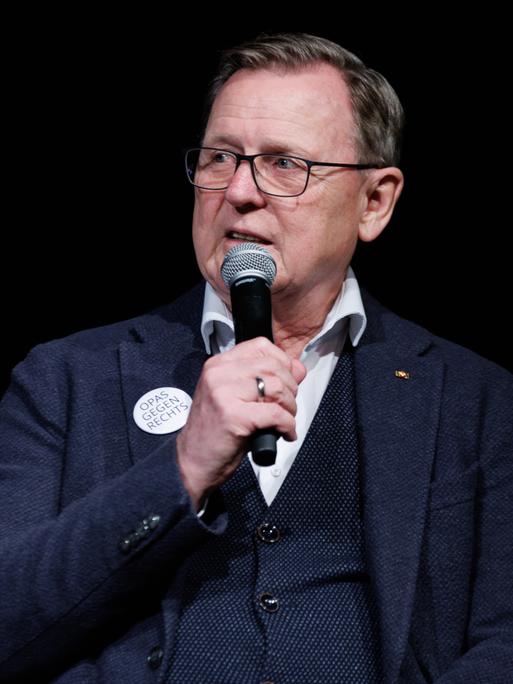 Der Ex-Ministerpräsident von Thüringen, Bodo Ramelow, sitzt bei einem Wahlkampfauftritt und hat ein Mikrofon in der Hand und hält dieses vor den Mund. 