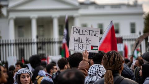 Pro-palästinensische Proteste vor dem Weißen Haus in Washington am 5. November 2023. Das Bild zeigt eine Menschenmenge, die vor einem Zaun steht. Im Hintergrund ist das Weiße Haus leicht verschwommen zu erkennen. Ein Demonstrant hält ein Schild mit der Aufschrift "Palestine will be free" in die Höhe.