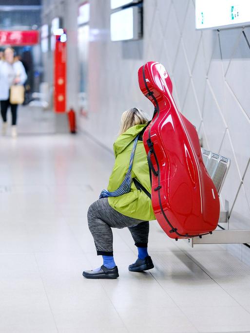 Ein Mensch mit einem roten Cello-Kasten sitzt in einer U-Bahnstation. 