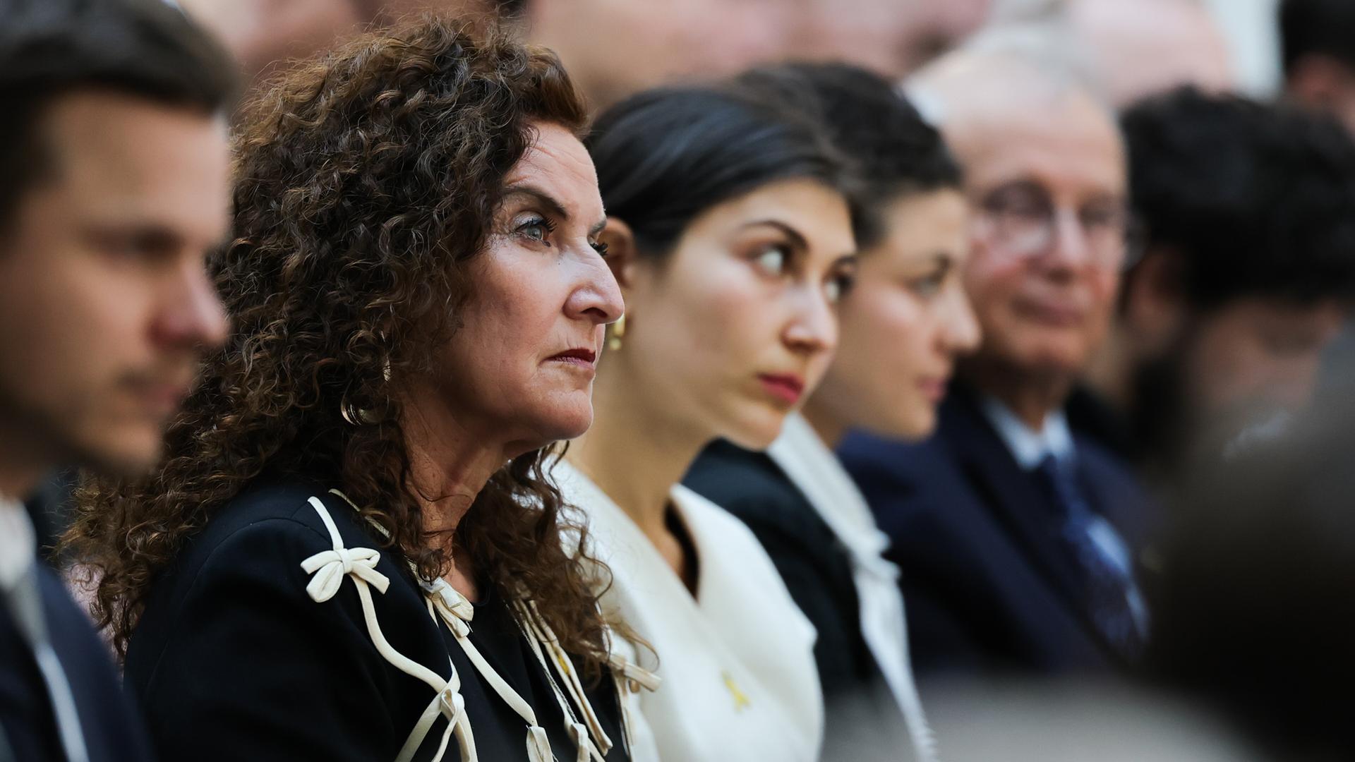 Ilana Lewitan (l), deren Vater Opfer der Shoah geworden ist, und ihre Töchtern Joelle und Lea sitzen bei einer Gedenkstunde für die Opfer des Nationalsozialismus. Sie trägt schwarze Kleidung und schaut nach vorne.