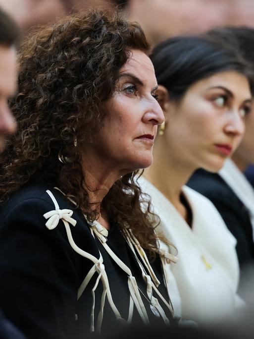 Ilana Lewitan (l), deren Vater Opfer der Shoah geworden ist, und ihre Töchtern Joelle und Lea sitzen bei einer Gedenkstunde für die Opfer des Nationalsozialismus. Sie trägt schwarze Kleidung und schaut nach vorne.