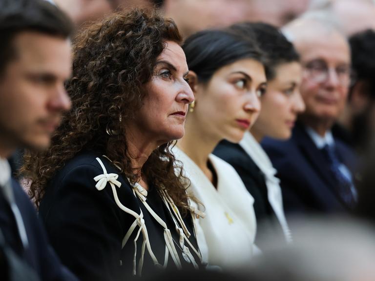 Ilana Lewitan (l), deren Vater Opfer der Shoah geworden ist, und ihre Töchtern Joelle und Lea sitzen bei einer Gedenkstunde für die Opfer des Nationalsozialismus. Sie trägt schwarze Kleidung und schaut nach vorne.