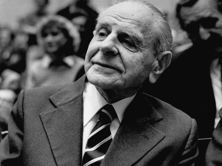 Karl Popper sitzt im Publikum einer Veranstaltung und hört aufmerksam zu