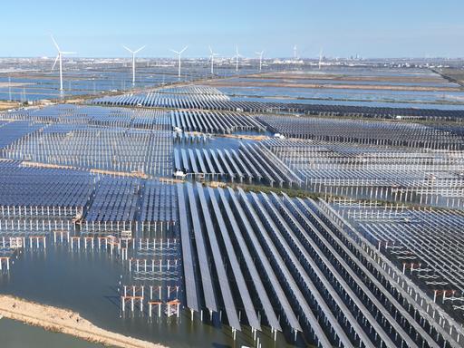 Zu sehen sind großflächige Solarmodule und mehrere Windkraftanlagen. Zu sehen sind großflächige Solarmodule und mehrere Windkraftanlagen.