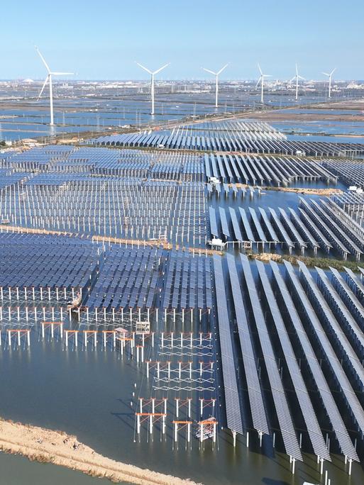 Zu sehen sind großflächige Solarmodule und mehrere Windkraftanlagen. Zu sehen sind großflächige Solarmodule und mehrere Windkraftanlagen.