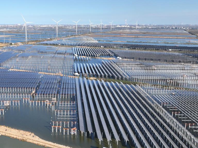 Zu sehen sind großflächige Solarmodule und mehrere Windkraftanlagen. Zu sehen sind großflächige Solarmodule und mehrere Windkraftanlagen.