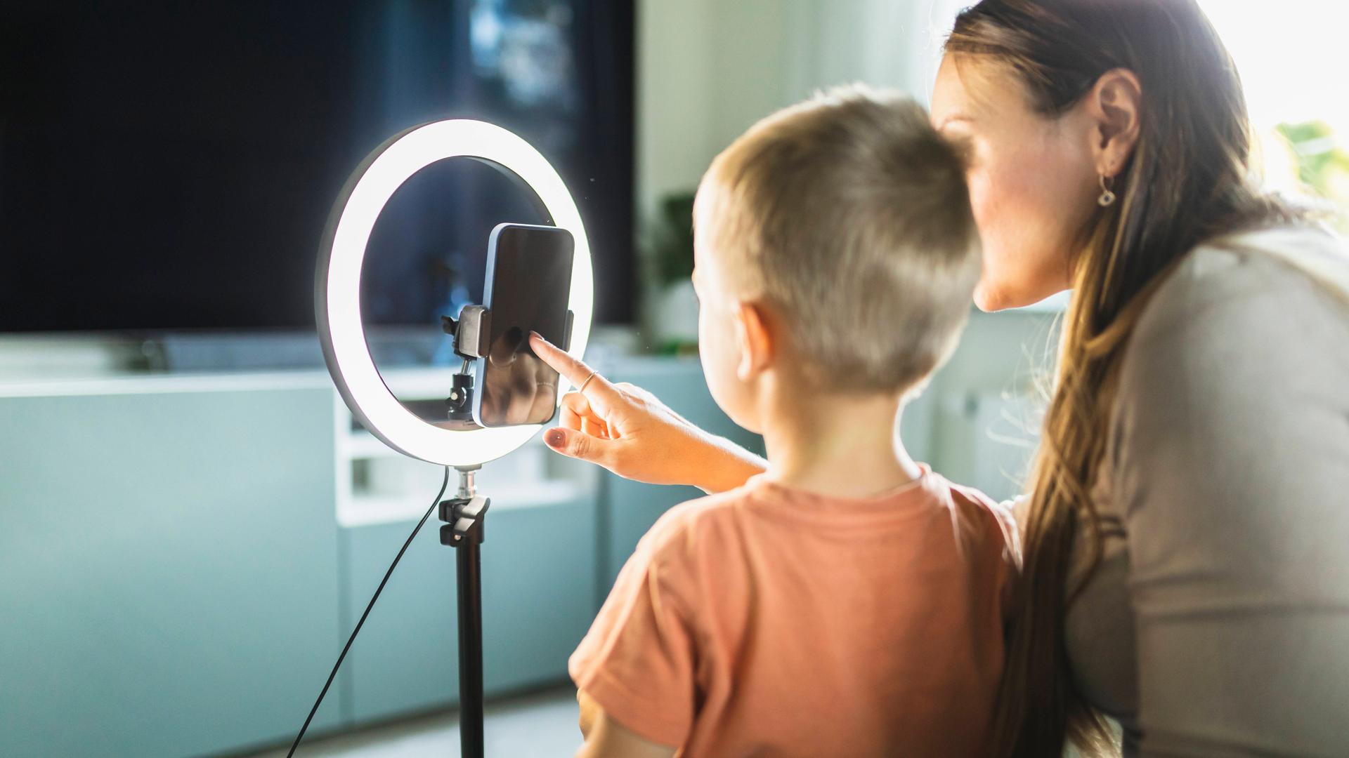 Eine Mutter steht gemeinsam mit ihrem Sohn vor einem Smartphone mit Ringlicht. Eine Mutter steht gemeinsam mit ihrem Sohn vor einem Smartphone mit Ringlicht.