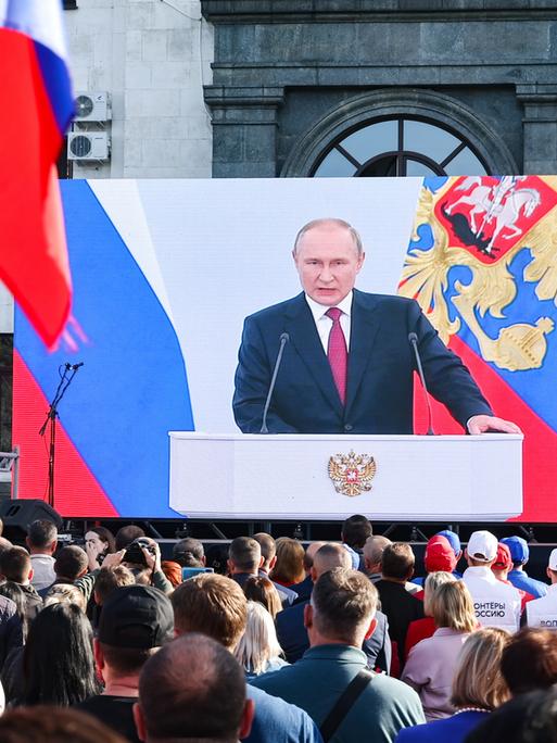 Auf einer großen Leinwand wird die Rede des russischen Präsidenten Wladimir Putin übertragen. Seine Anhänger stehen davor.