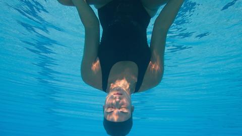 Eine Frau kopfüber unter Wasser in Meditationshaltung.