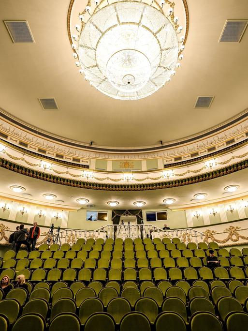 Blick in den festlich erleuchteten Zuschauersaal des Theaters von Mariupol mit grünen Sitzreihen und einem Kronleuchter