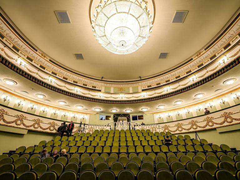 Blick in den festlich erleuchteten Zuschauersaal des Theaters von Mariupol mit grünen Sitzreihen und einem Kronleuchter