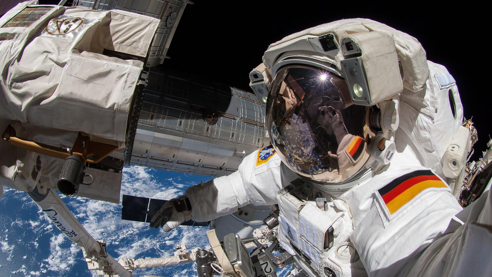 Ein Astronaut mit deutschem Hoheitsabzeichen auf seinem Raumanzug arbeitet außerhalb der ISS im Weltraum. 
