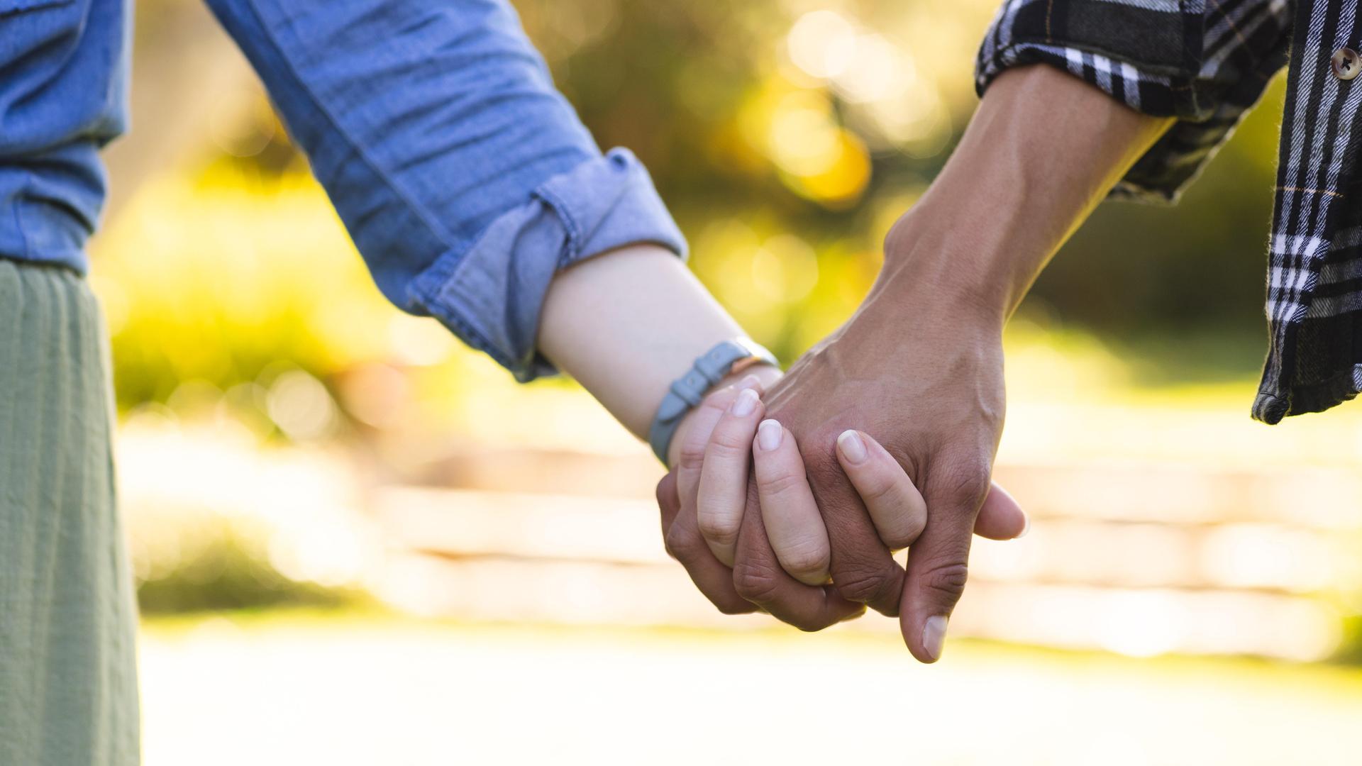 Blick auf die Hände eines Pärchens, das Hand in Hand spazieren geht. (Symbolbild)