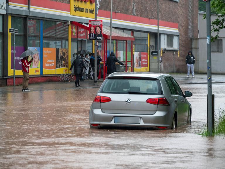 Passanten stapfen und fahren durch das Hochwasser in der Fischbachstraße in Saarbrücken. Nach starken Regenfällen steht diese teilweise unter Wasser.