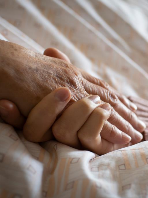 Eine Frau hält die Hand einer Pflegebedürftigen