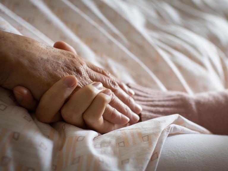 Eine Frau hält die Hand einer Pflegebedürftigen