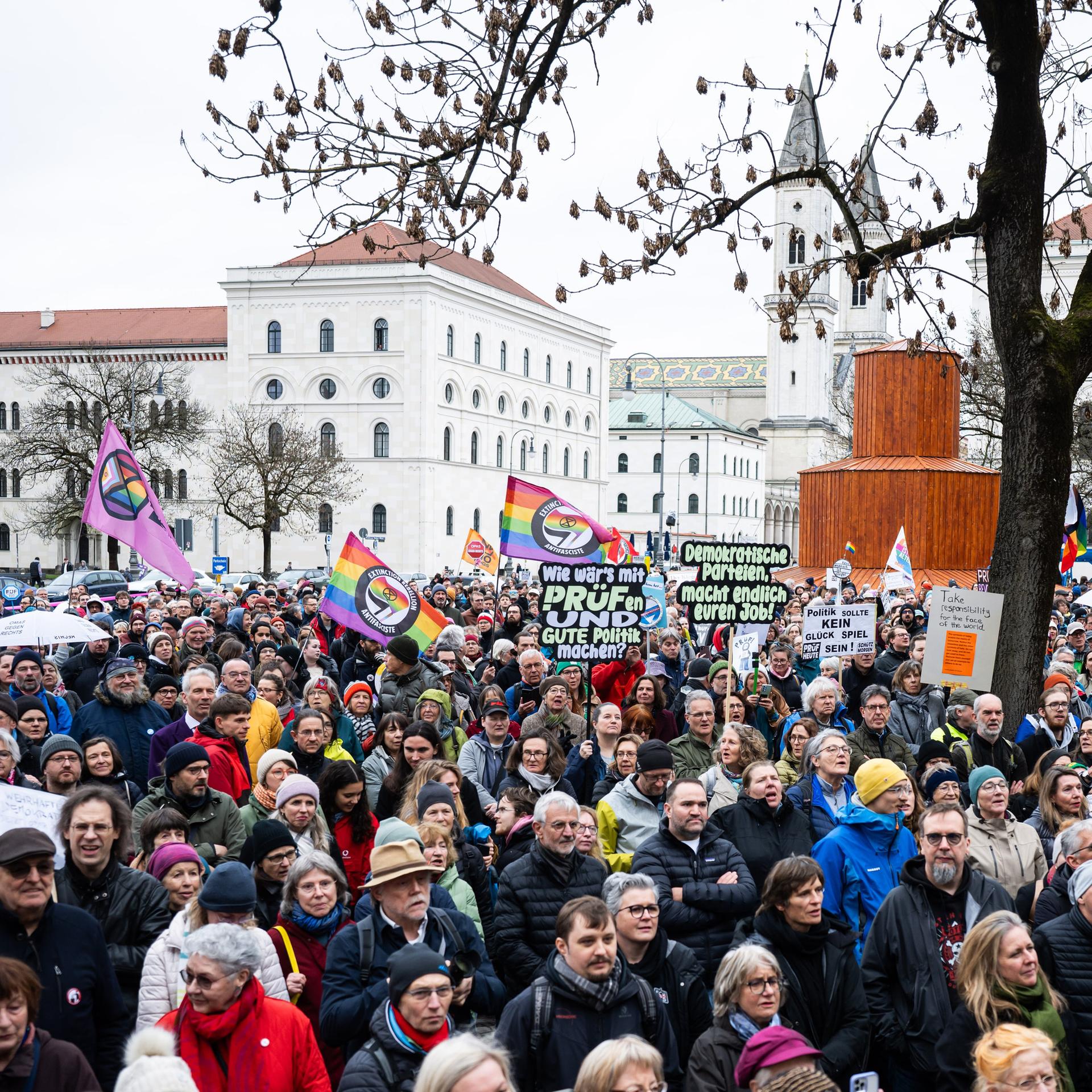 Teilnehmer der Demo für die Überprüfung rechtsextremer Parteien durch das Bundesverfassungsgericht stehen mit Plakaten und Schildern auf dem Geschwister Scholl Platz.