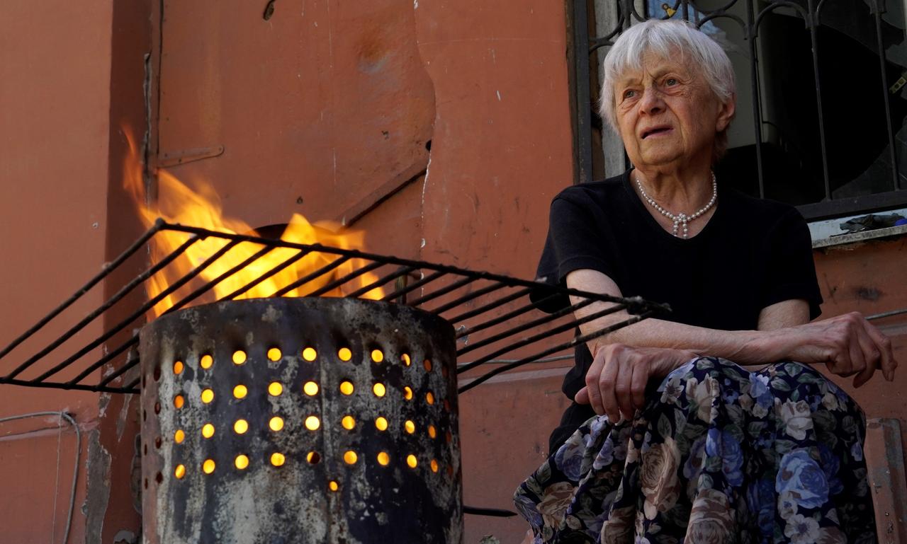 Eine Frau sitzt vor ihrem Haus in Mariupol und hat ein Feuer zum Kochen angezündet.