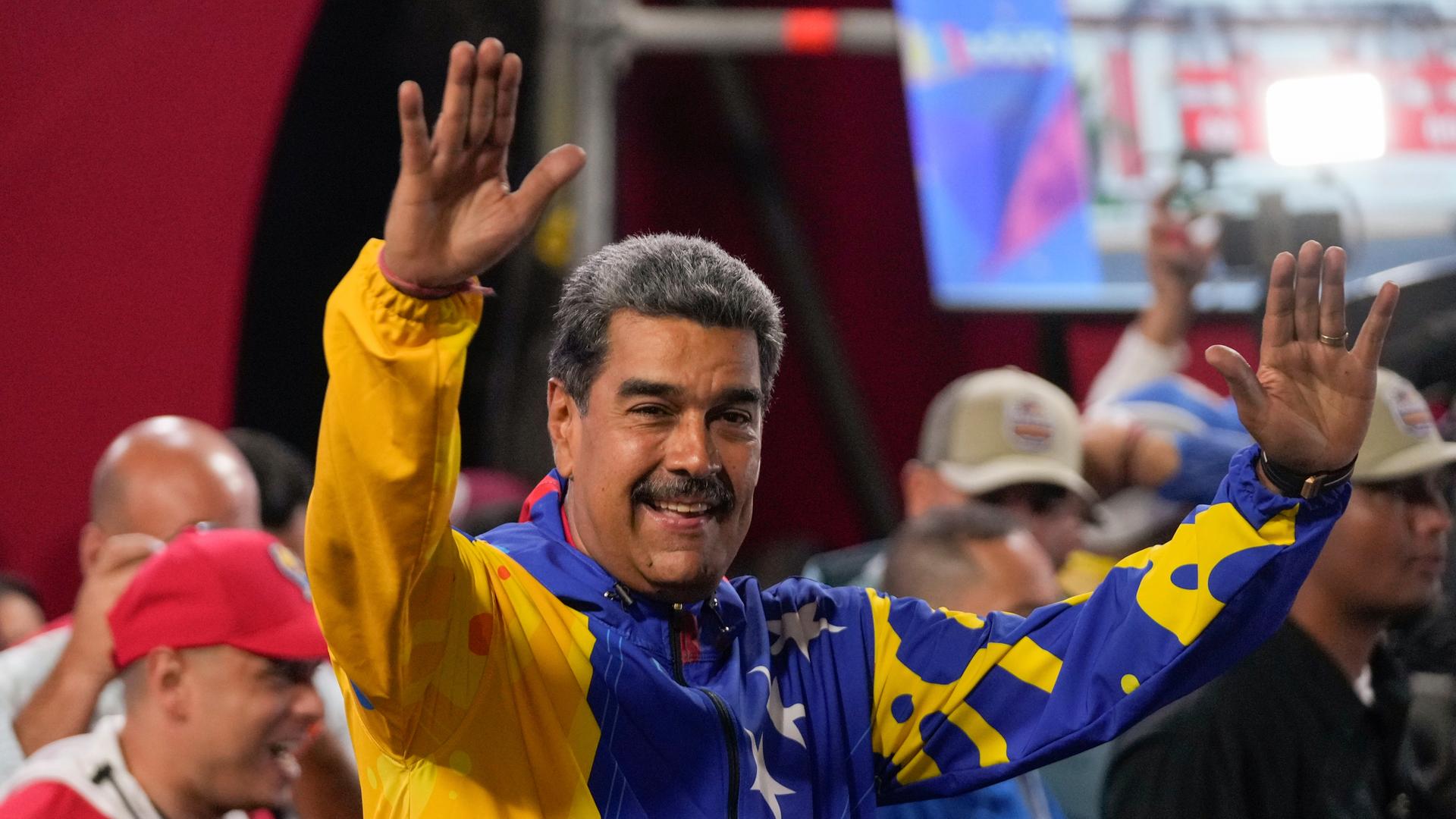 Venezuelas Präsident Nicolas Maduro hat beide Hände gehoben und lächelt.